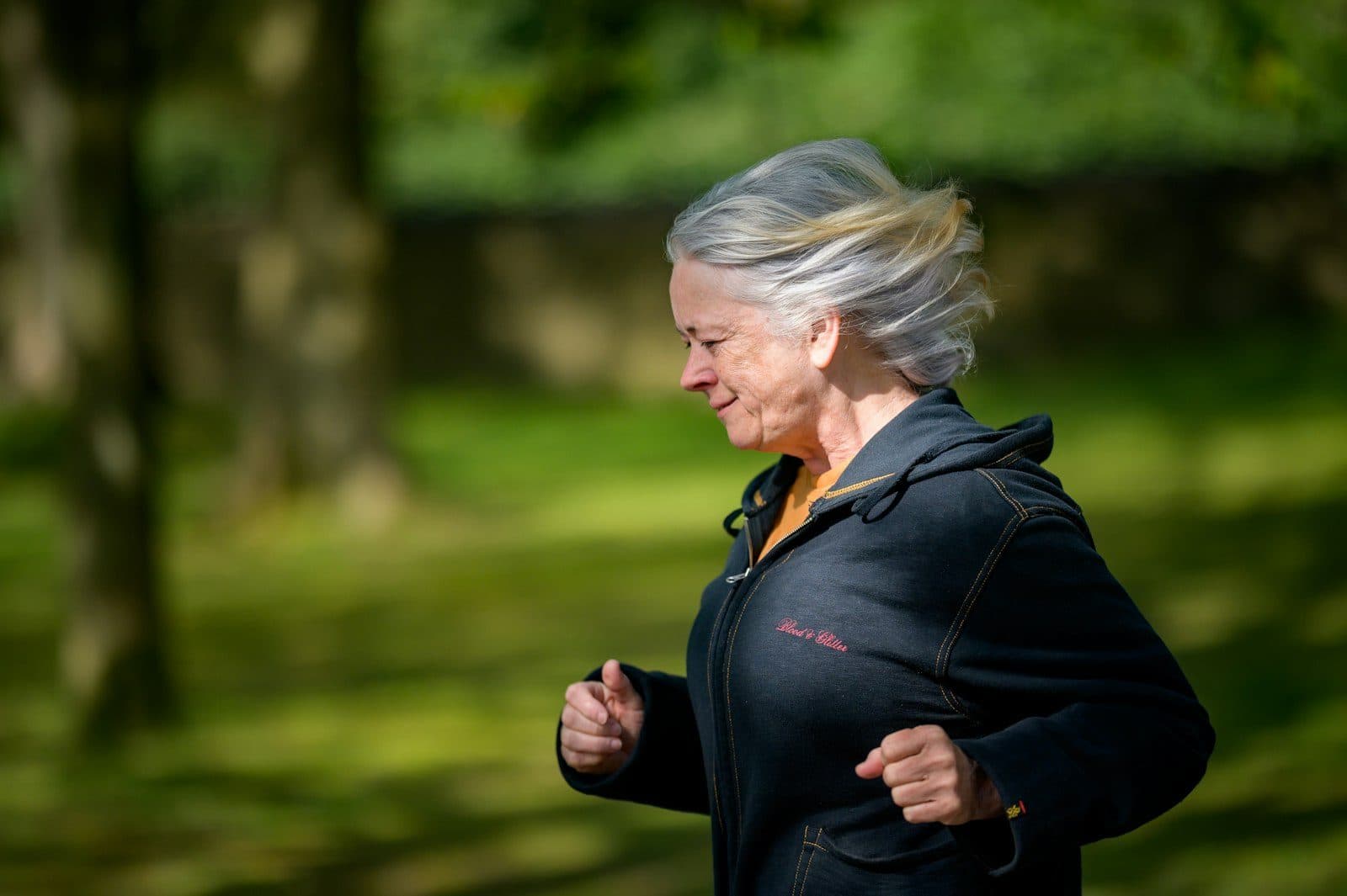 An older woman jogging along a path in a green park